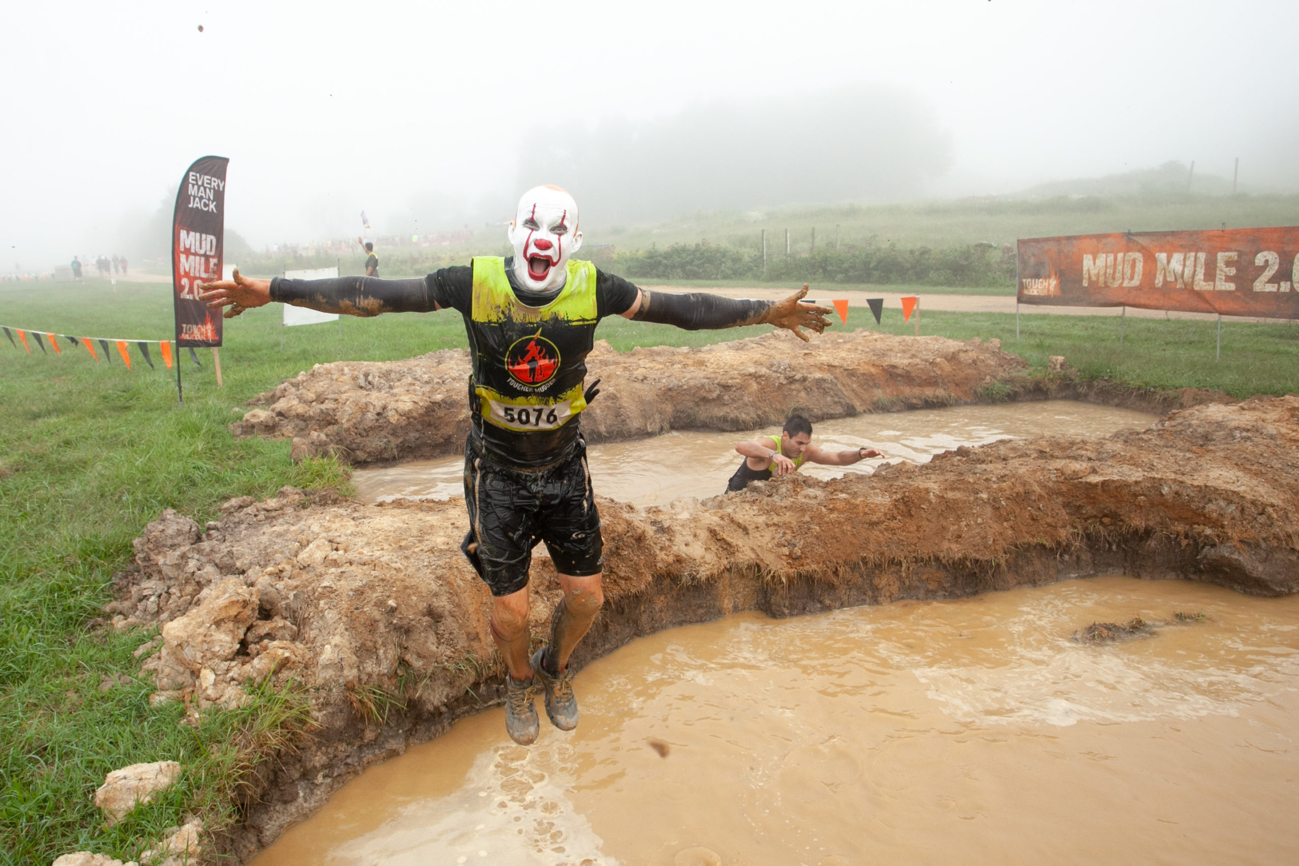 Participant with clown makeup jump in the mud
