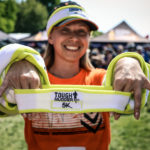 Volunteer smiling while showing the Tough Mudder headband in the camera