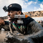 Participants crawling through mud with Tough Mudder Challenges logo