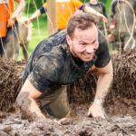 Participant crawling in the mud to avoid wires of Electroshock Therapy