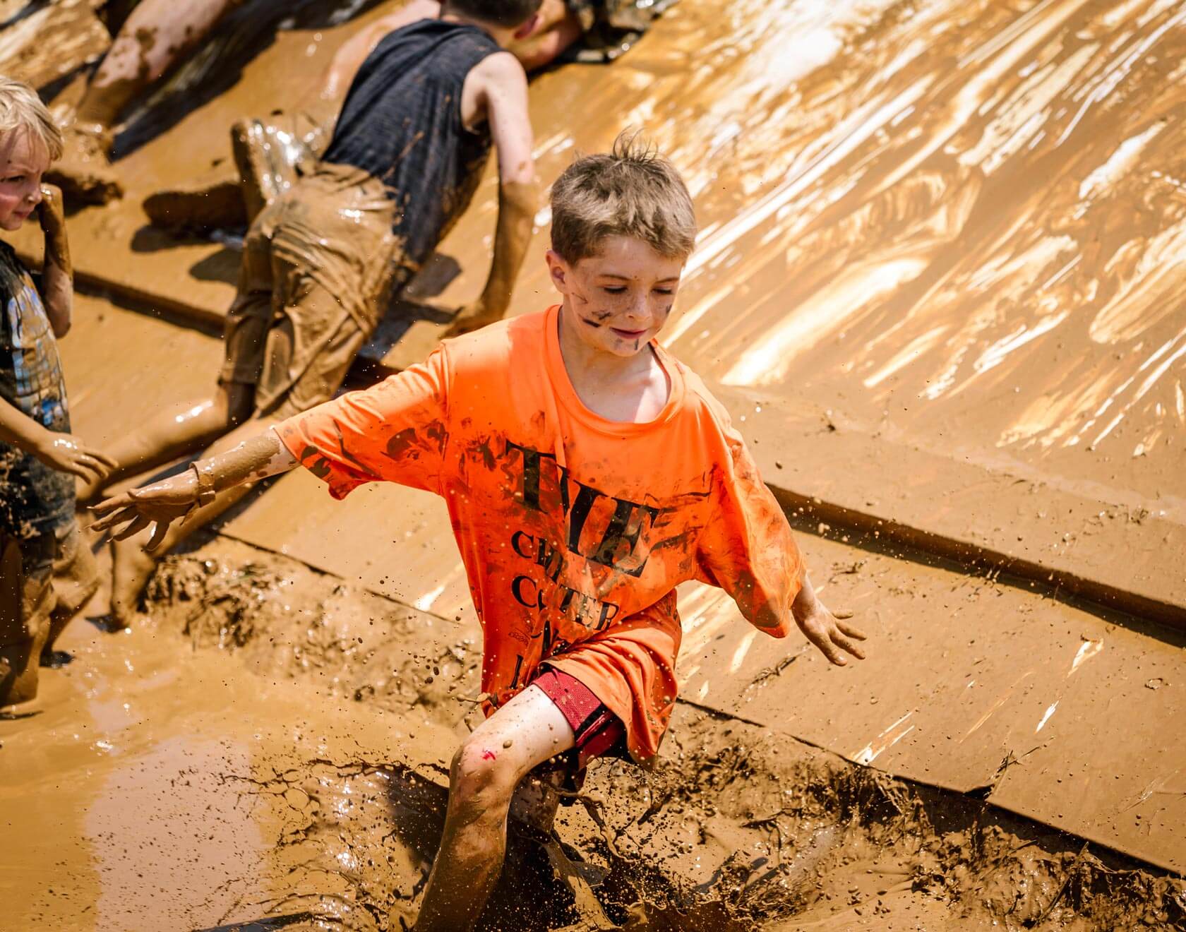Kid participant in orange shirt walking in the mud