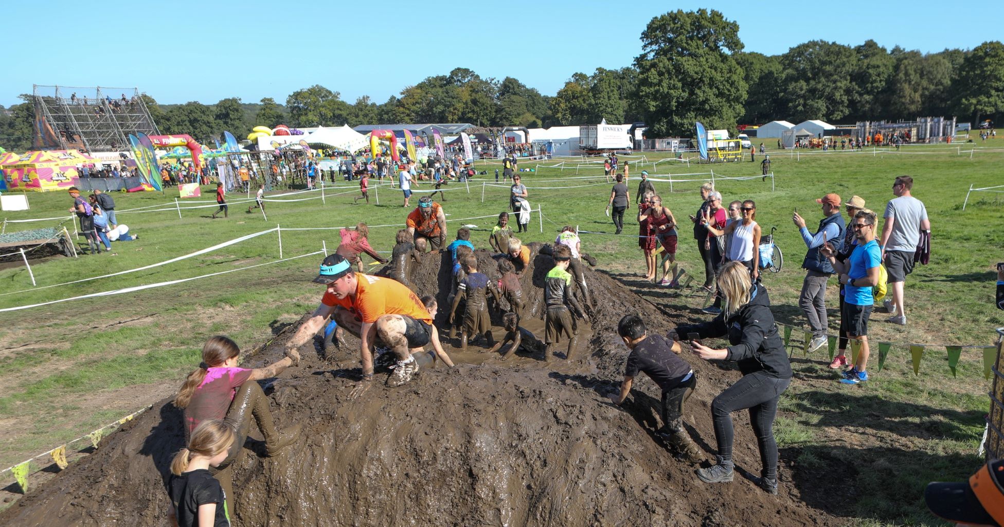 Adults helping kid participants climb a mud hill