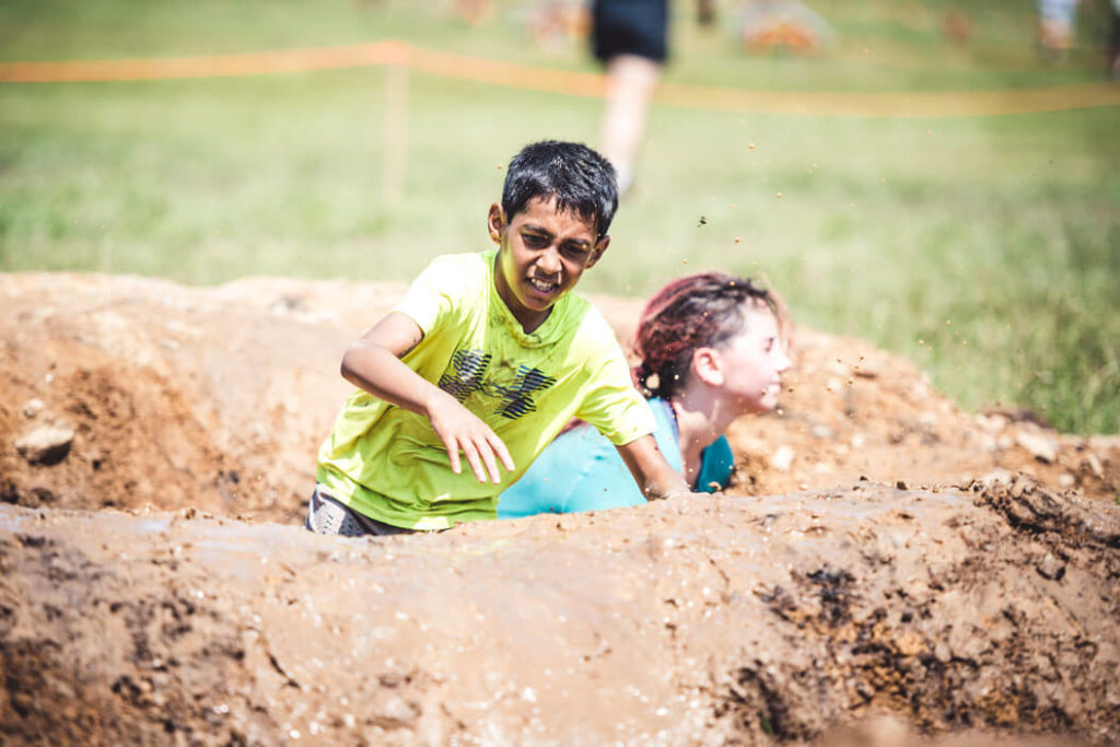 Two kid participants hardly climbing a mud hill
