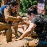 Participant holding her teammate's hand to get up in the ground