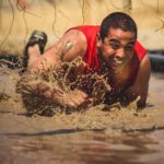 Participant laughing while crawling in the mud to avoid electric wires
