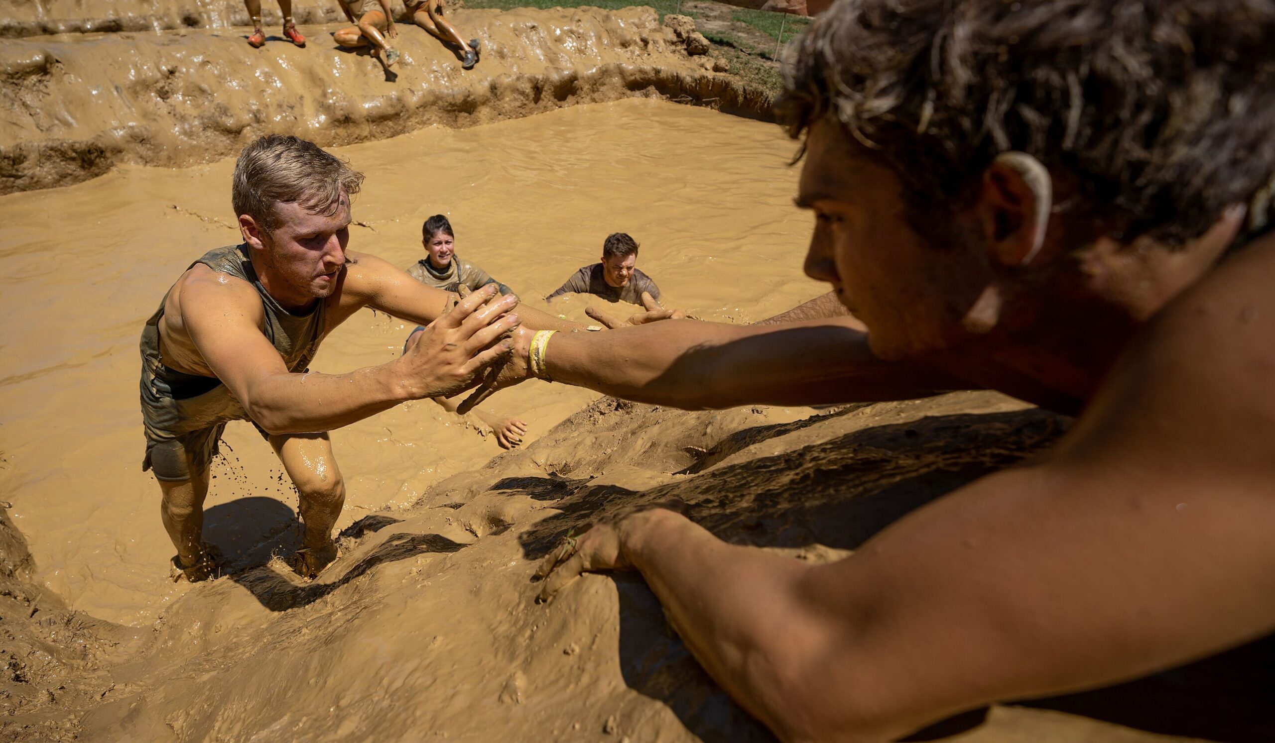 Participant lending his hand for his teammate to cling to as he climb the mud hill