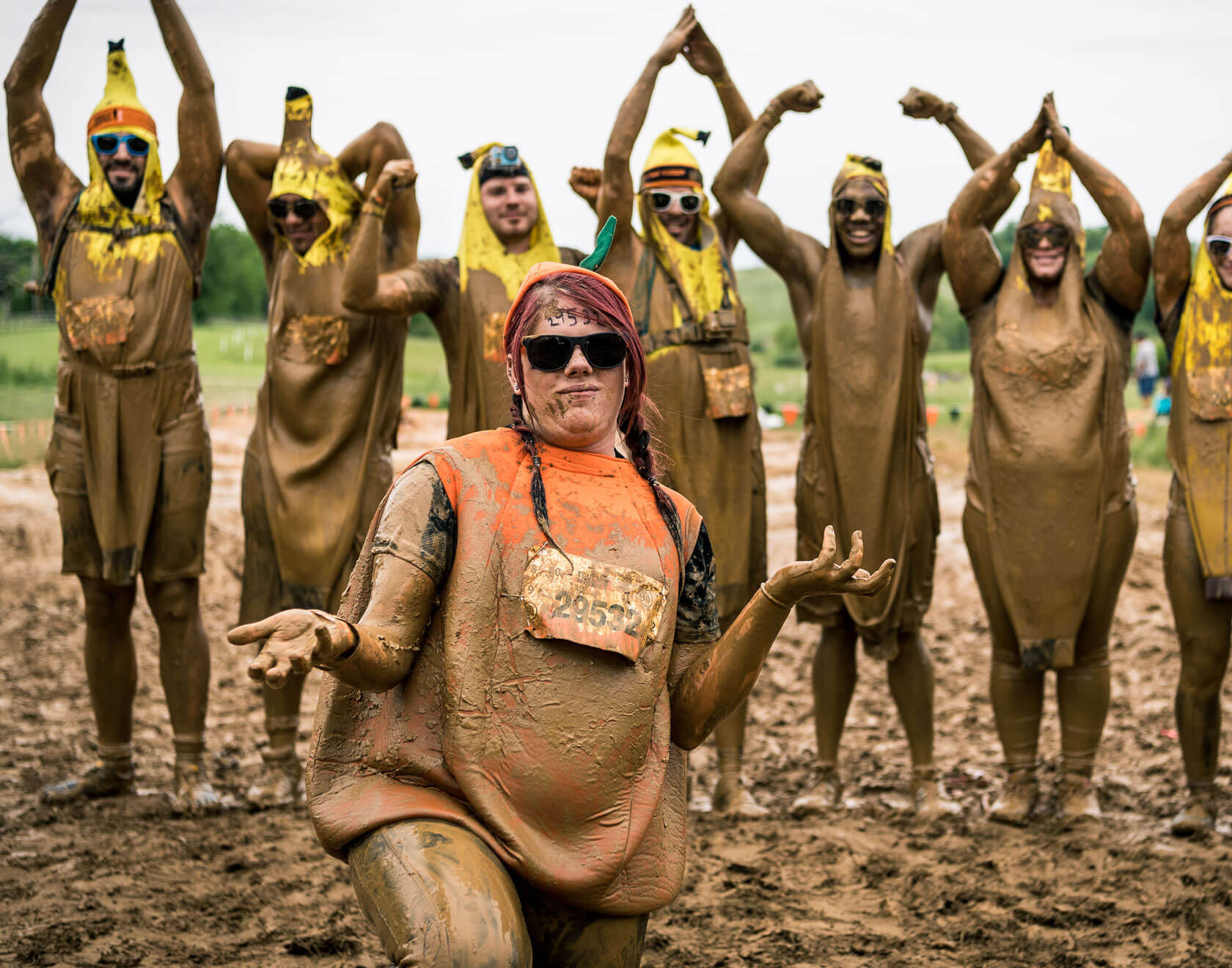 Participants in banana outfit standing behind a kneeling participant wearing orange outfit