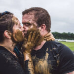 Muddy couple kissing in field.