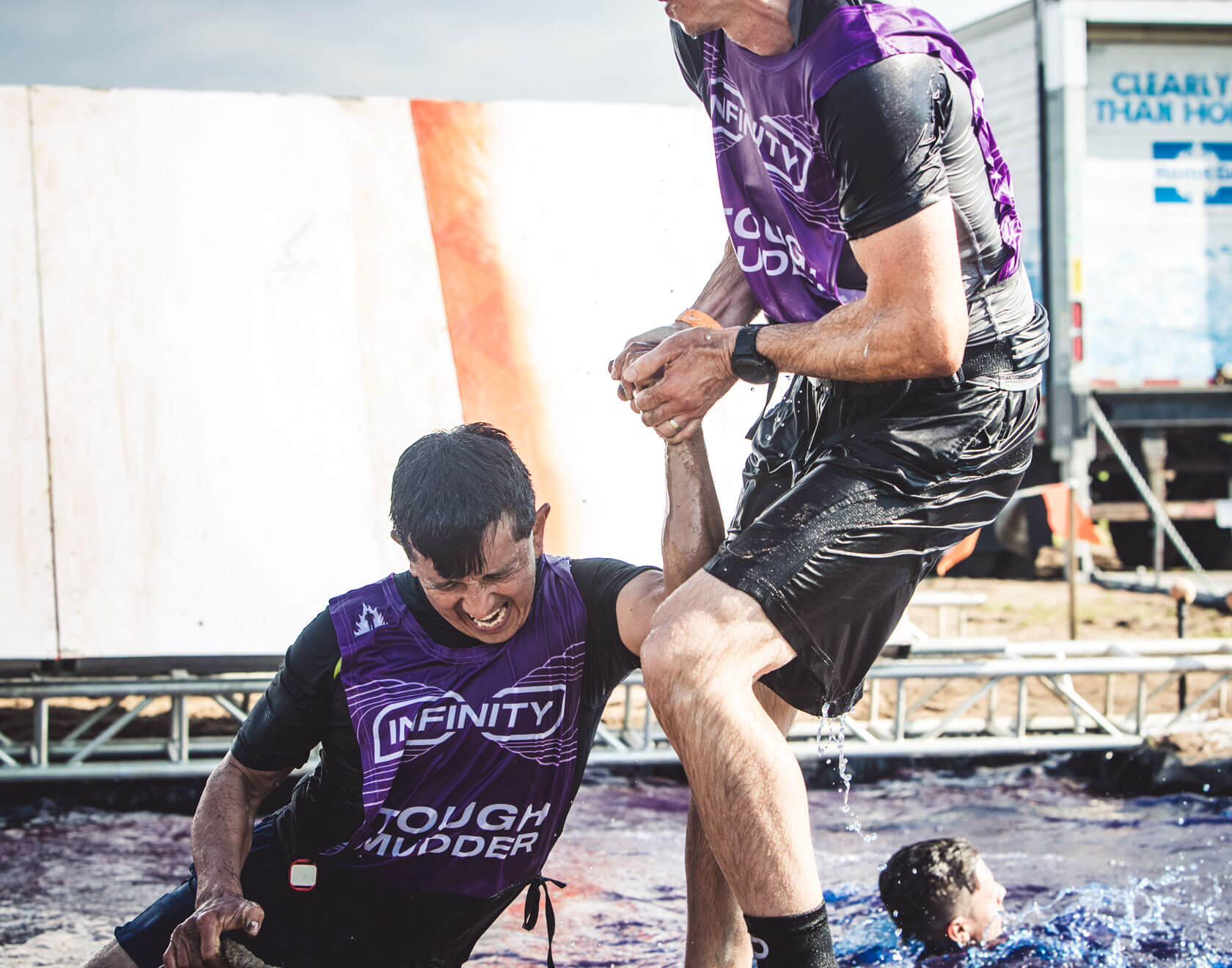 A mudder helping his teammate get up from falling