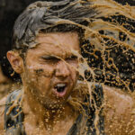Man in muddy water doing a Tough Mudder obstacle and grimacing.