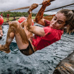 A mudder holding tightly on a rope to avoid falling in the water