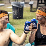 Two people sharing cans of beer as celebratory for finishing Tough Mudder obstacle course