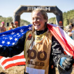 Woman holding the American flag and smiling widely at the finish line