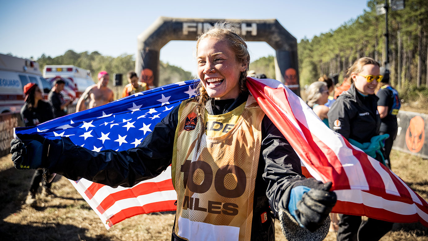 Woman holding the American flag and smiling widely at the finish line