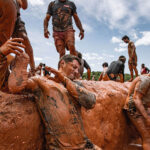 men covered in mud as they help each other to conquer Mud Mile